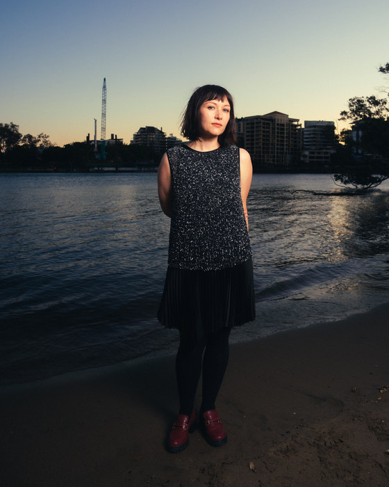 Leah Kardos standing on the riverbank at dusk in a sequinned dress, 2024