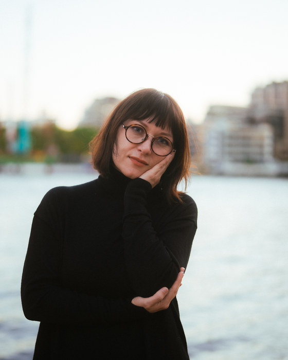 Leah Kardos in a black turtleneck resting her chin on her hand by the river, 2024