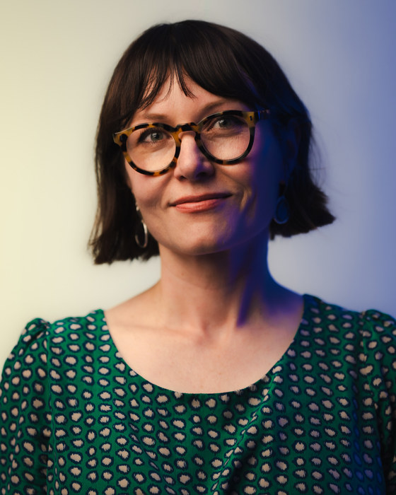 Leah Kardos in a green patterned dress against a yellow and blue gradient backdrop, 2026